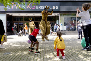 A person dressed as a kangaroo jumps with children on a sunny street